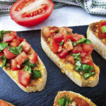 Featured image for the post. A close up image fo the finished bruschetta on a black platter.