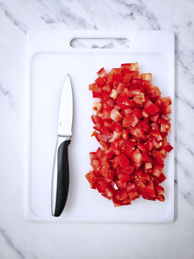 Diced tomatoes in a white chopping board with a knife beside