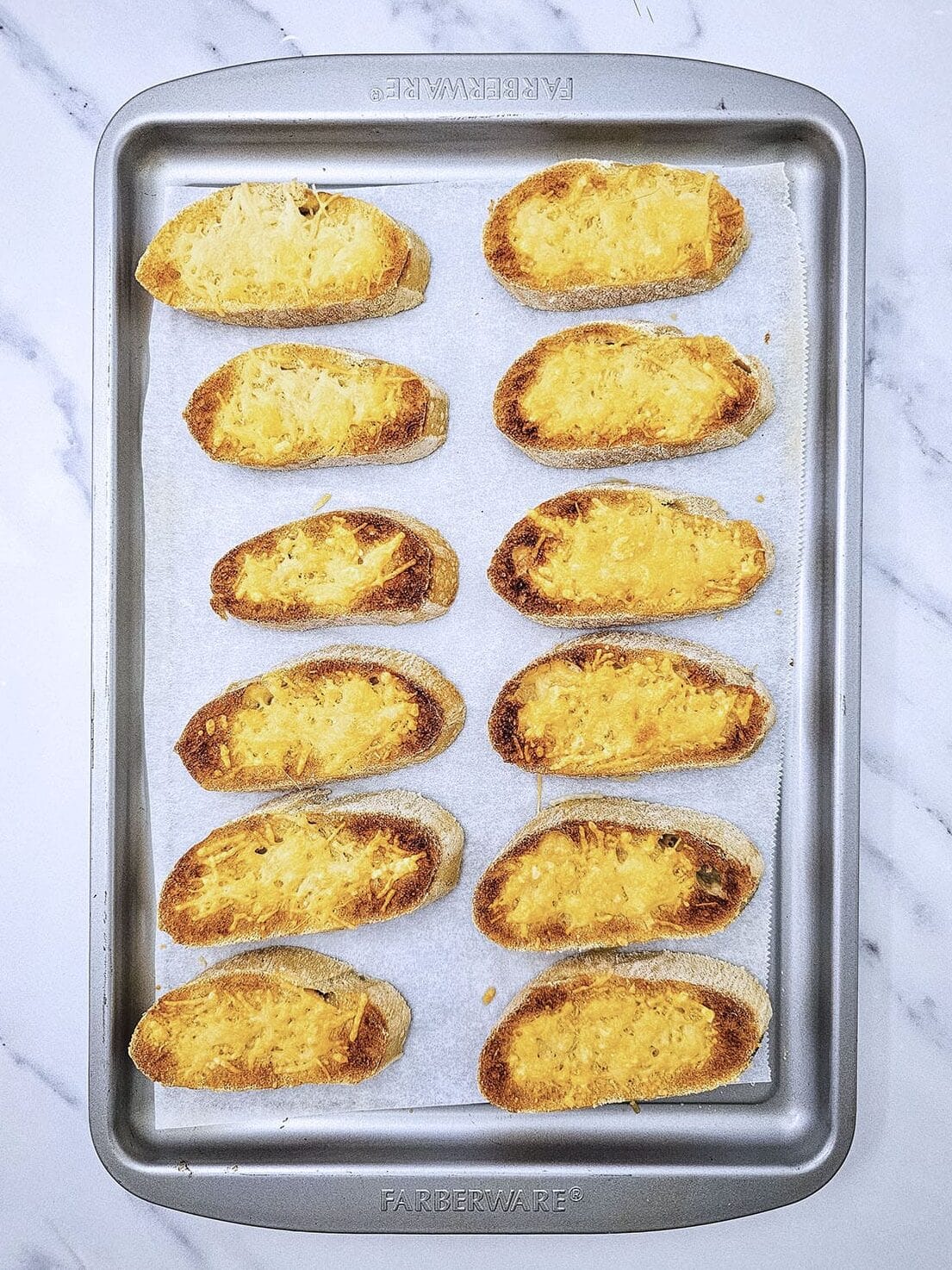 Toasted slices of bread topped with arranged on a metal baking sheet.