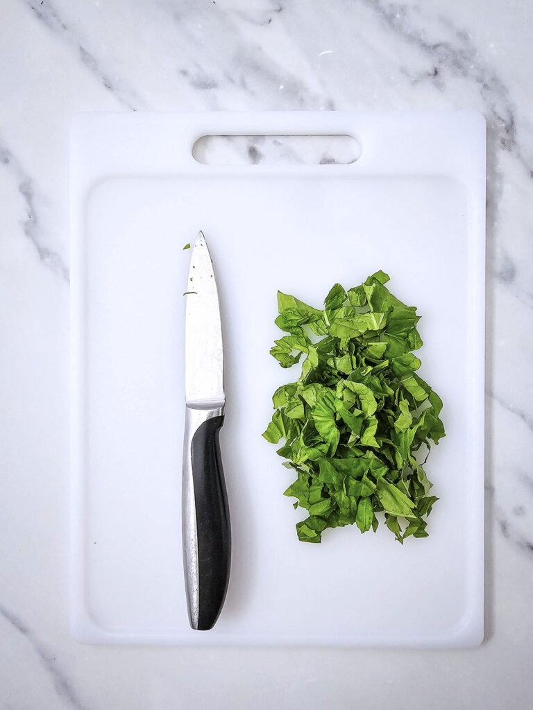 chopped basil in a white chopping board with a knife beside