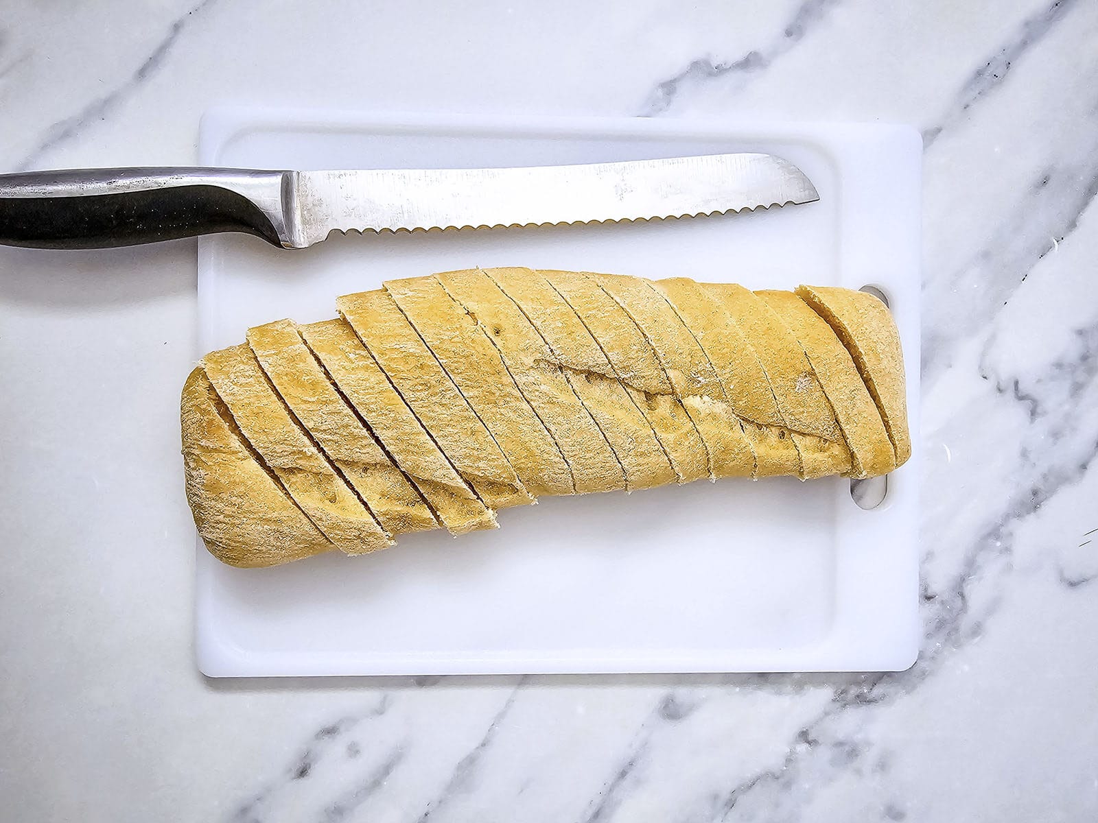 sliced baguette on a white chopping board and a bread knife beside it
