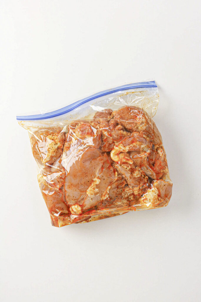 Raw chicken marinating inside a sealed plastic bag.