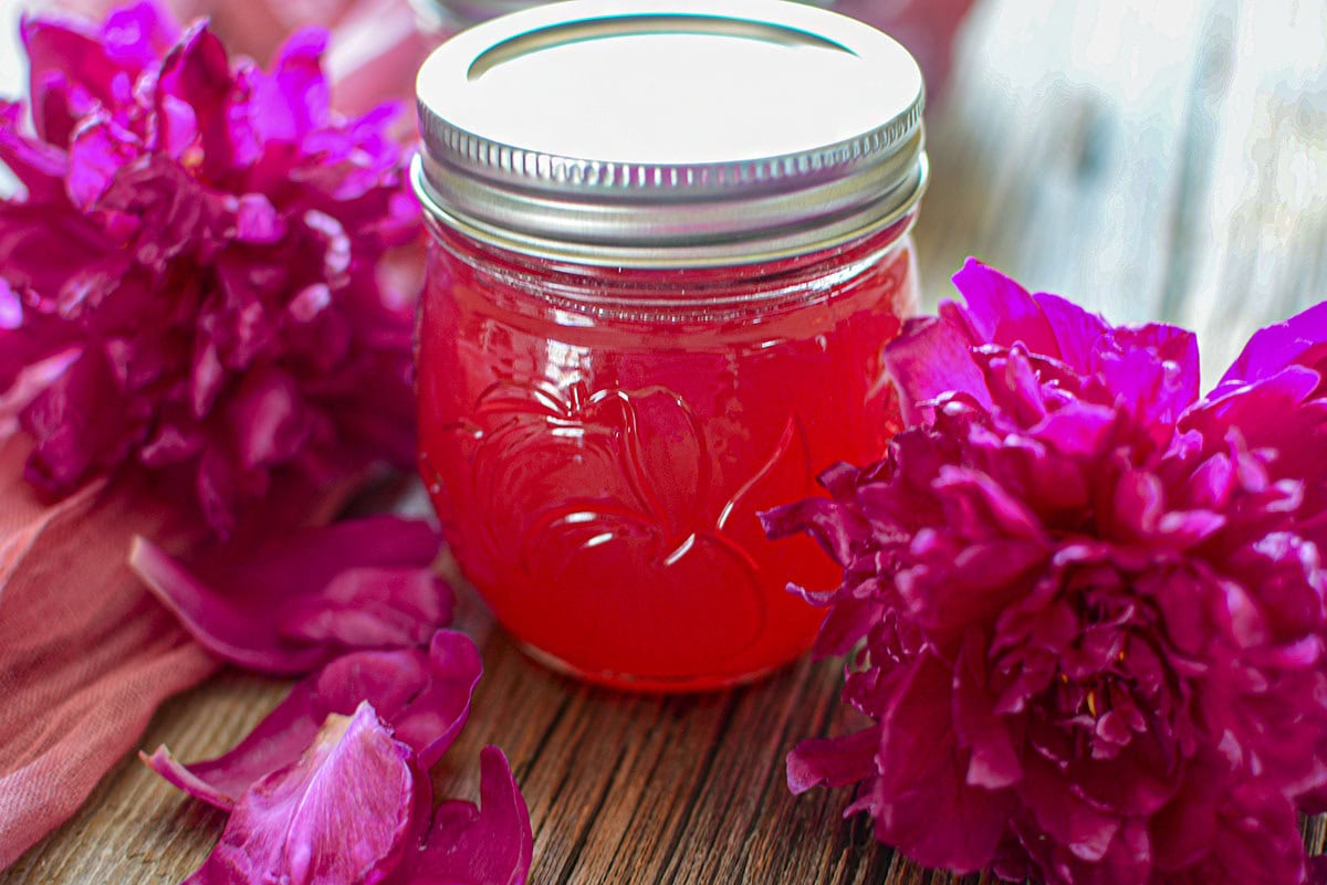 Peony Jelly in a glass jar with flowers on either side of it.