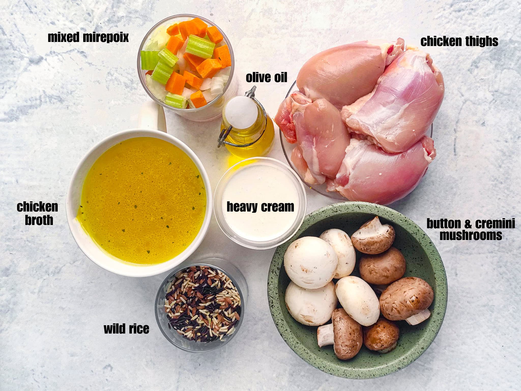 Raw ingredients for soup arranged on a counter, including chicken thighs, mushrooms, wild rice, broth, cream, and chopped vegetables.