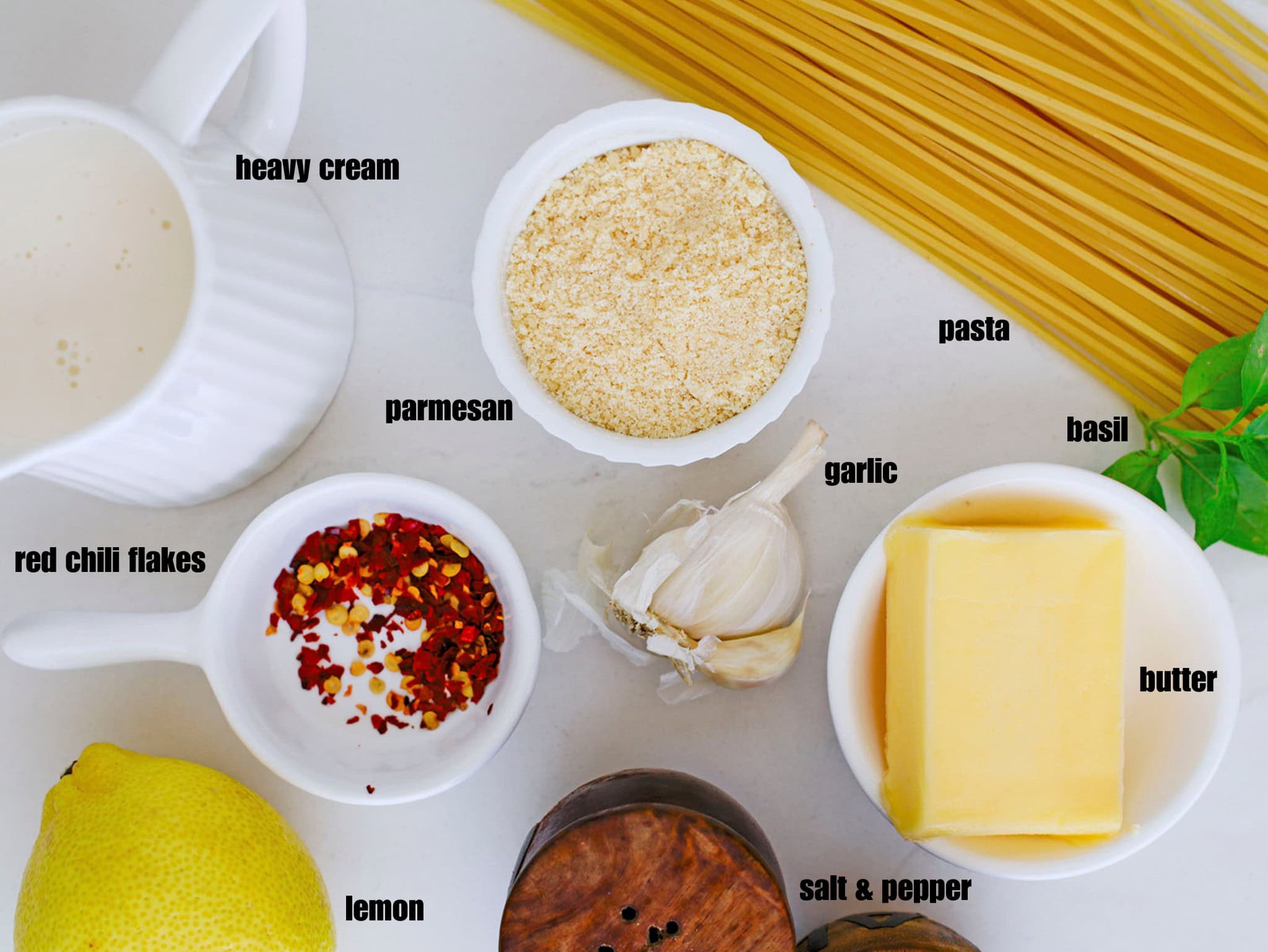 A flat lay of raw pasta ingredients, including butter, garlic, a lemon, butter, cream, and dry noodles on a counter.