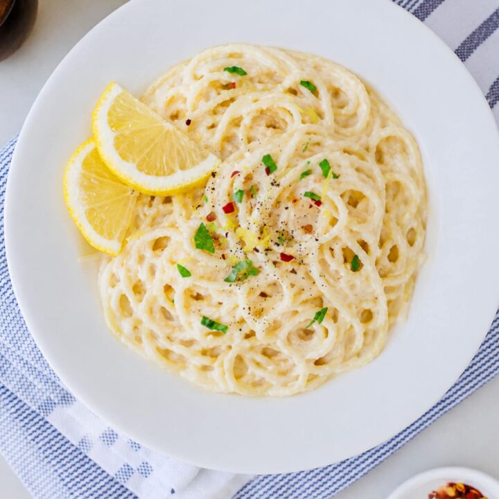Lemon garlic pasta in a white bowl with lemon wedges on the side.