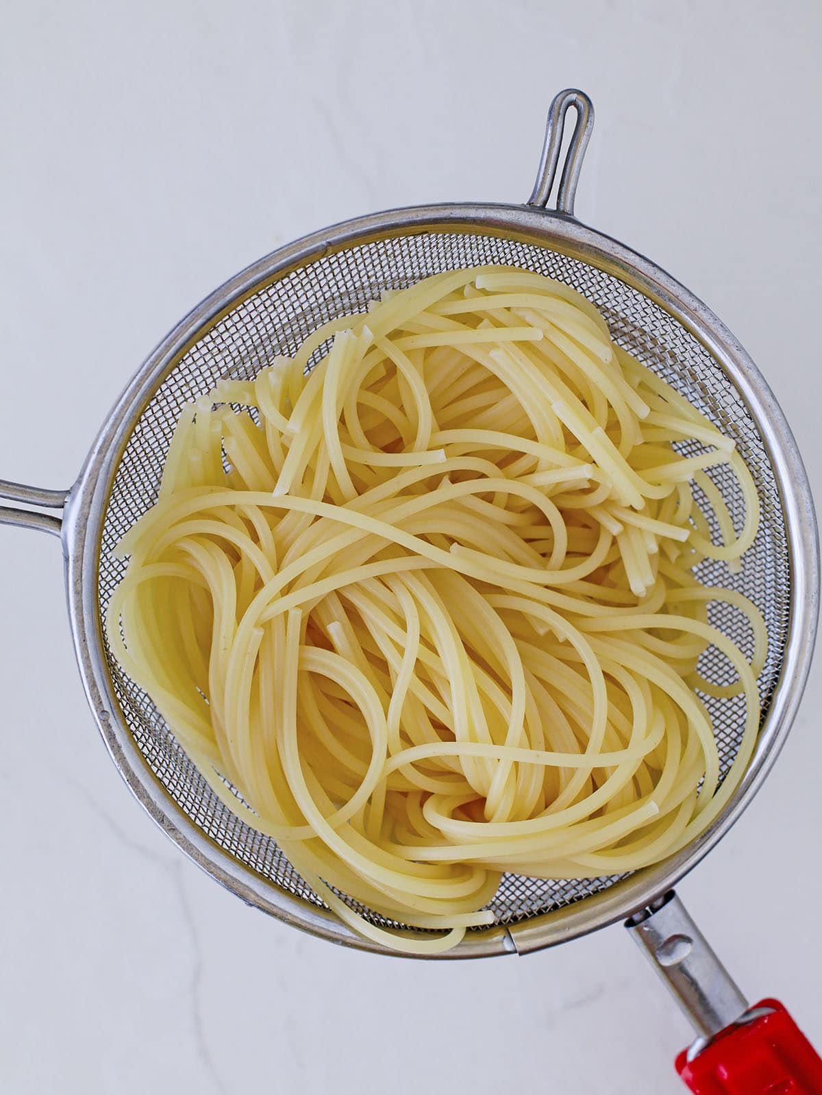 shot of cooked long pasta draining inside a metal strainer.