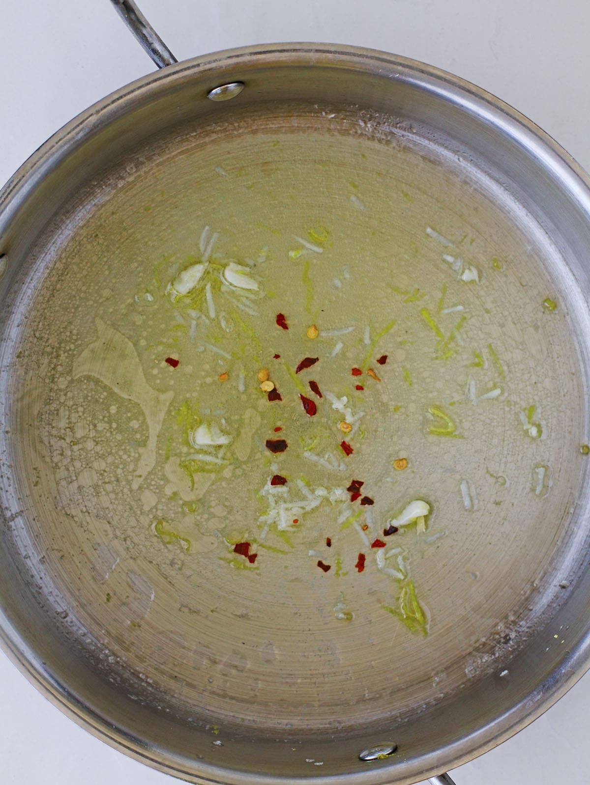 Spices, garlic, and butter warming in the bottom of a stainless steel skillet.