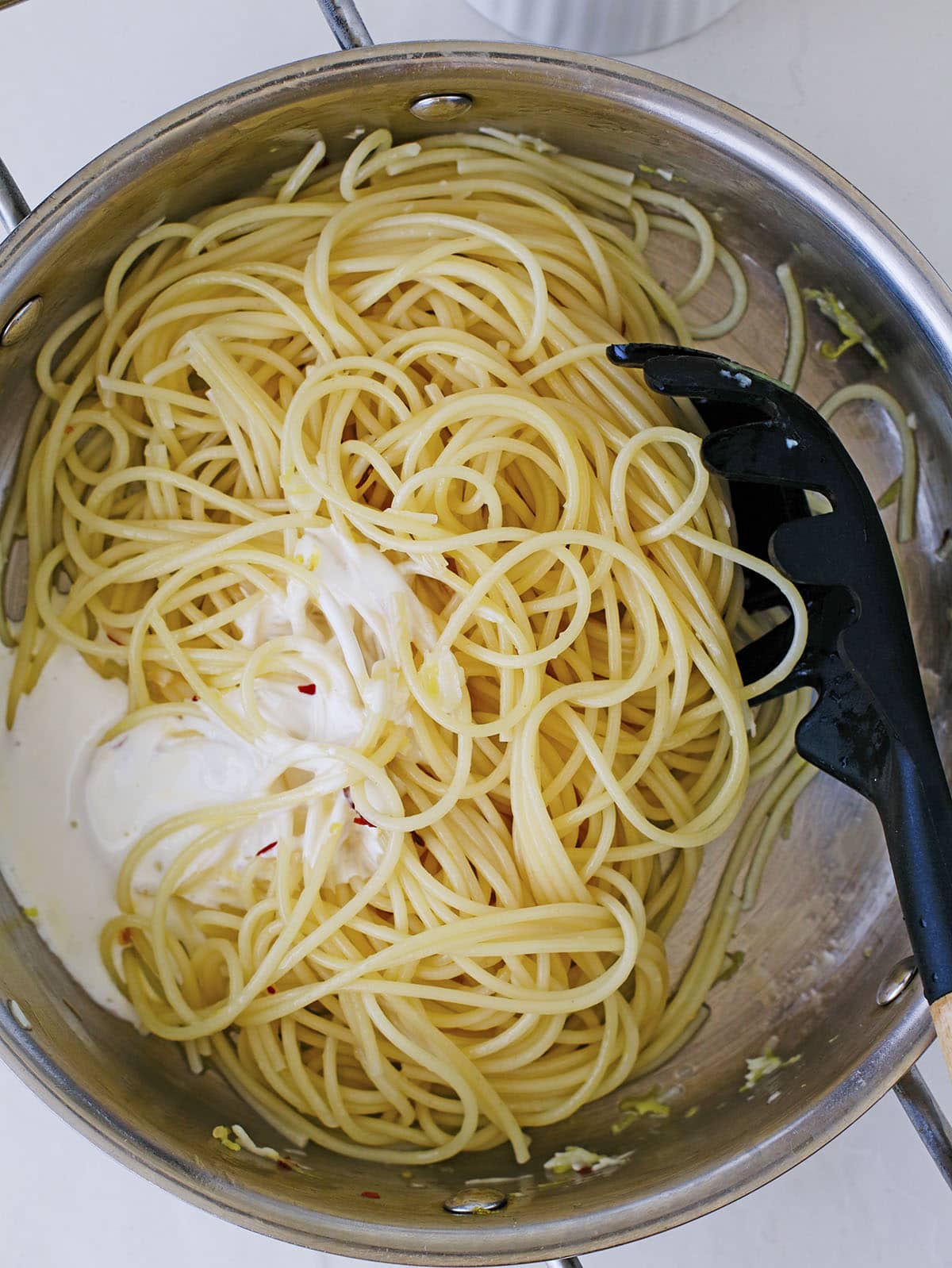 Unmixed cream sauce sitting on top of cooked spaghetti noodles in a pan.
