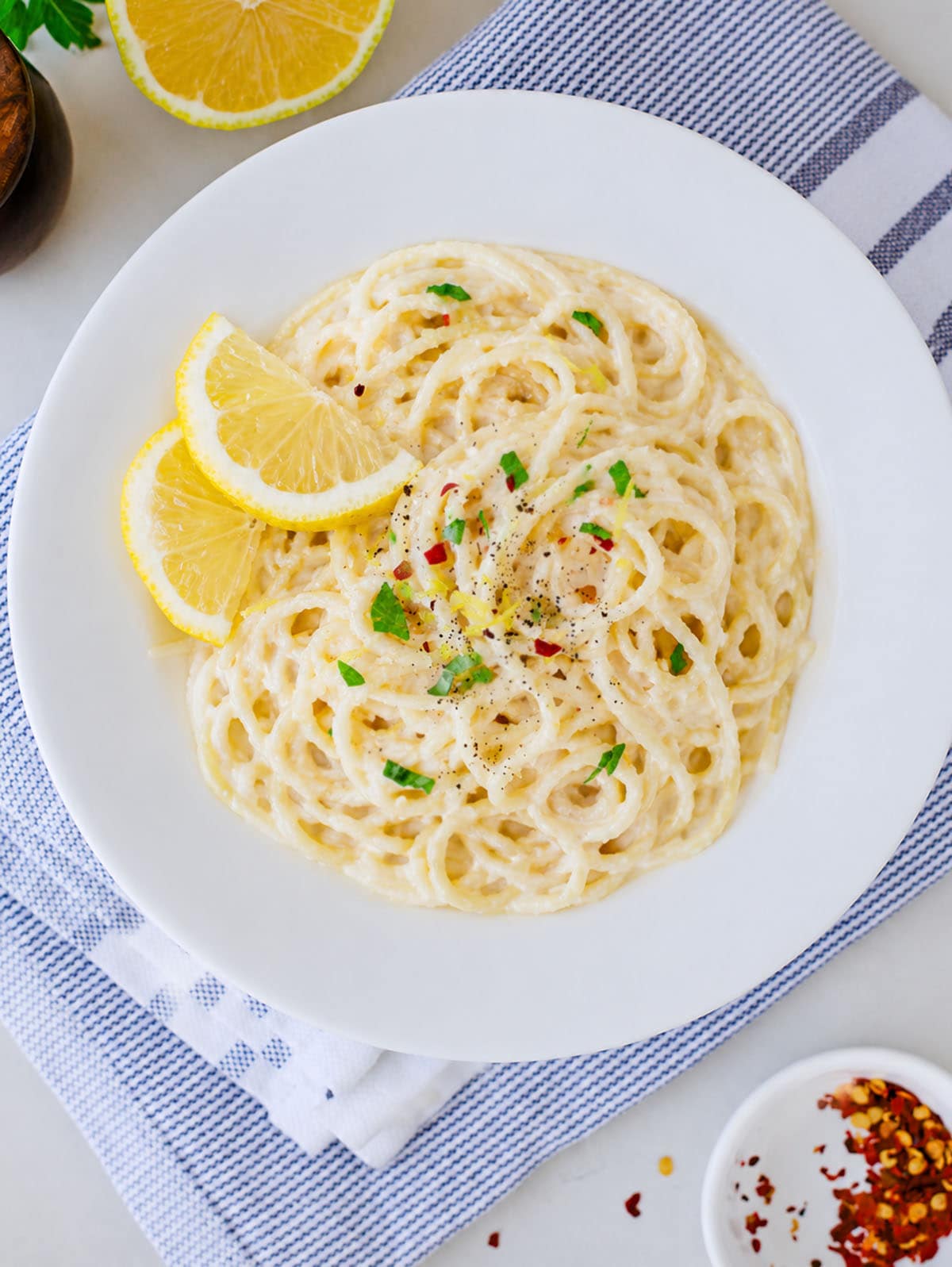 Lemon garlic pasta in a white bowl with lemon wedges on the side.