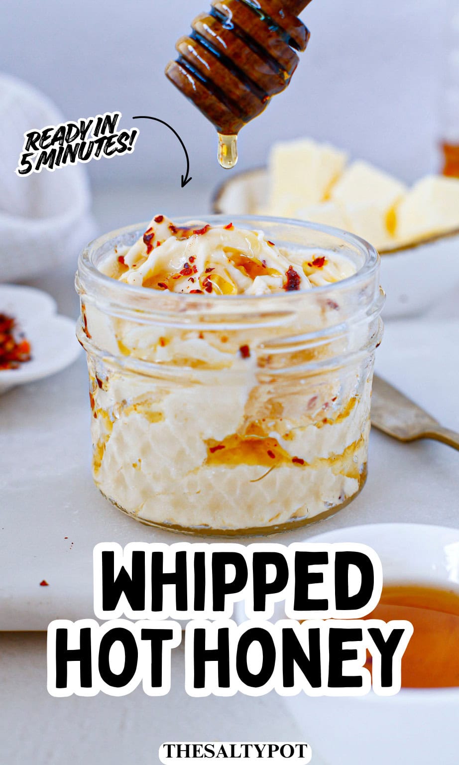 A glass jar filled with whipped honey butter, topped with red pepper flakes and a honey drizzle