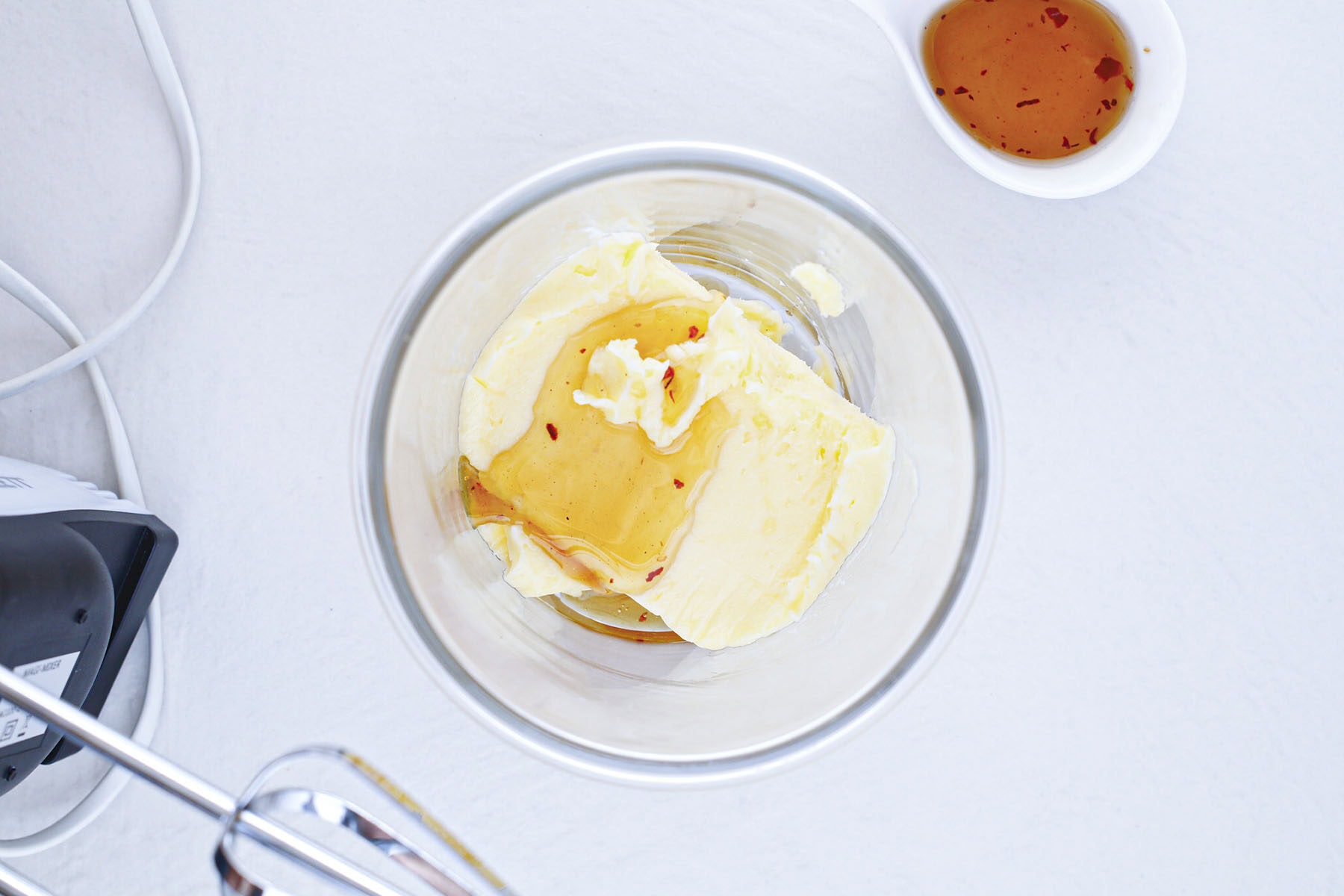 Honey drizzled over a block of butter inside a glass mixing bowl.