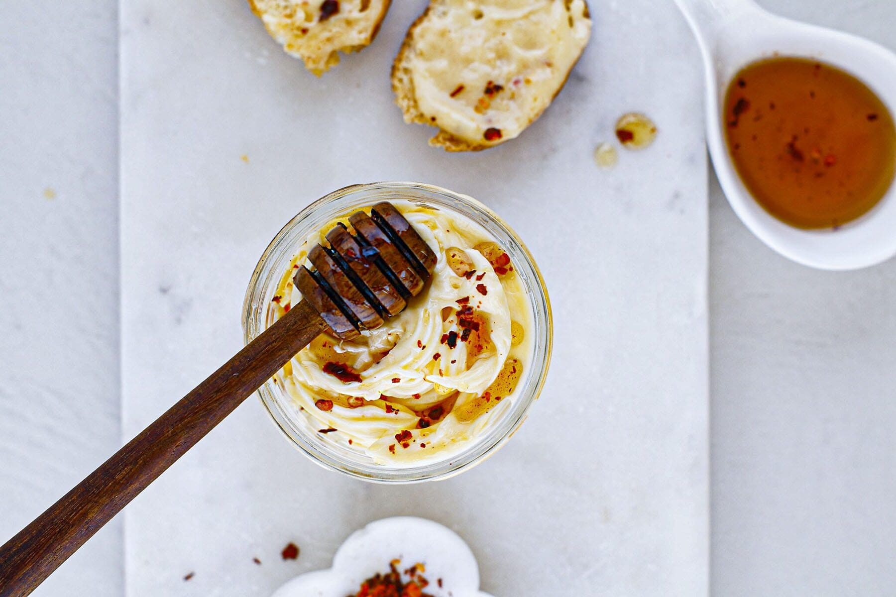 Overhead view of a glass jar filled with whipped spread, a honey dipper resting inside.
