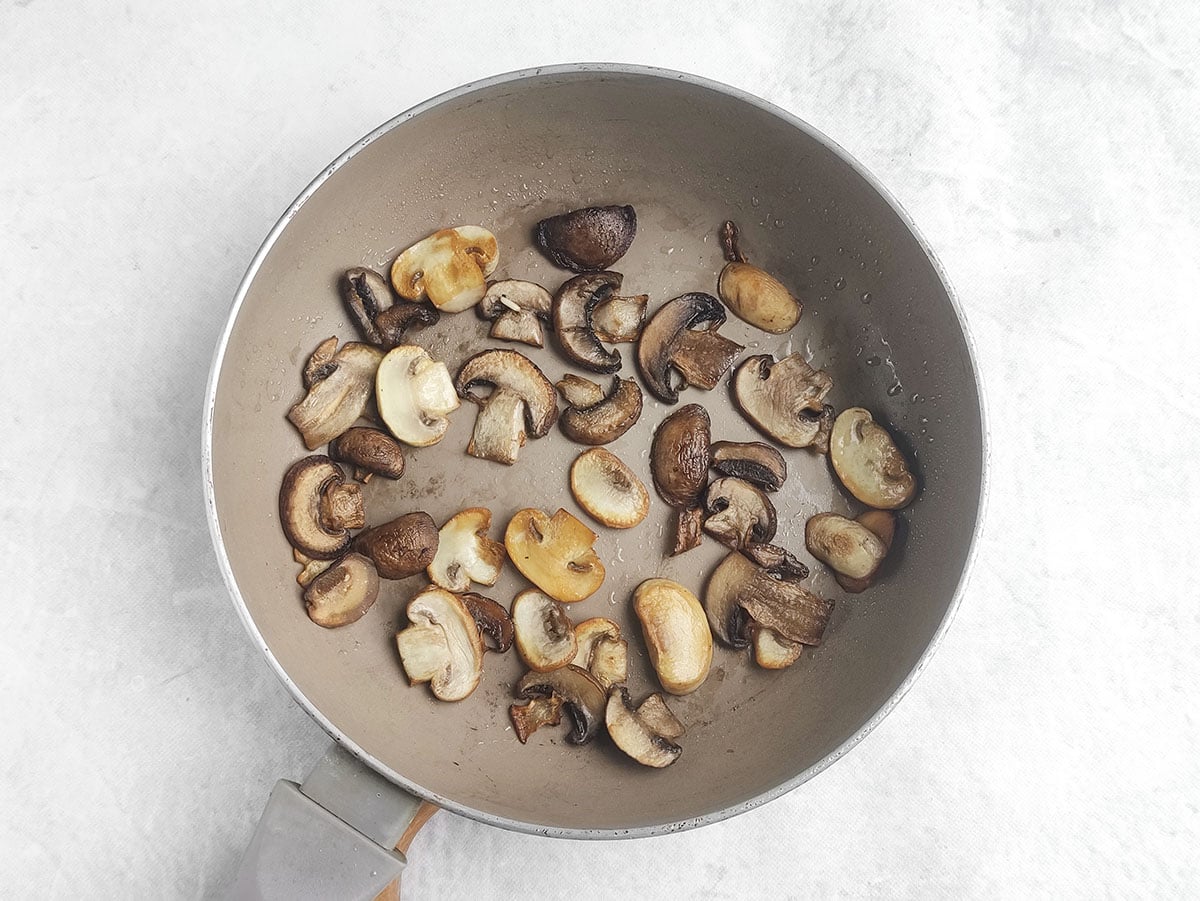 Sliced mushrooms being sautéed in a frying pan.
