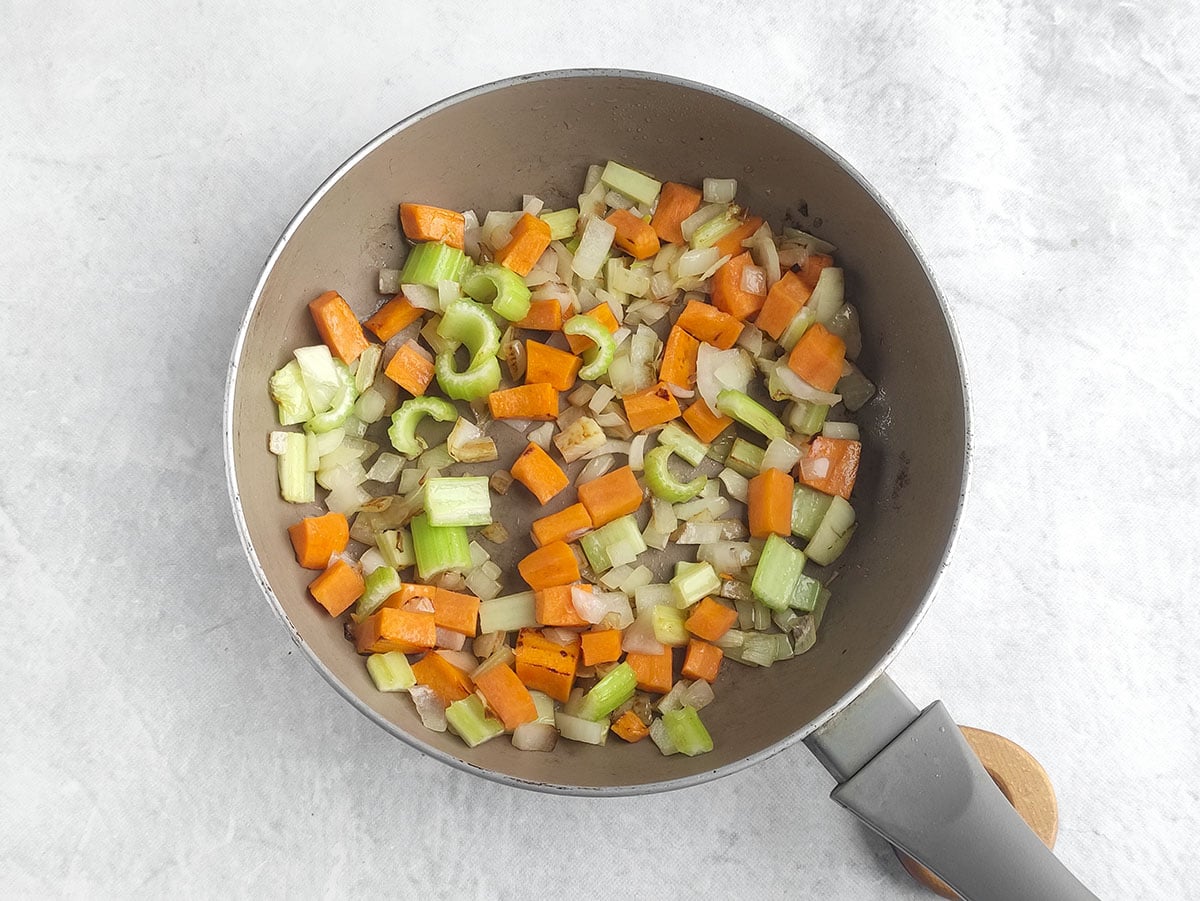 Chopped carrots, celery, and onions being sautéed in a frying pan.
