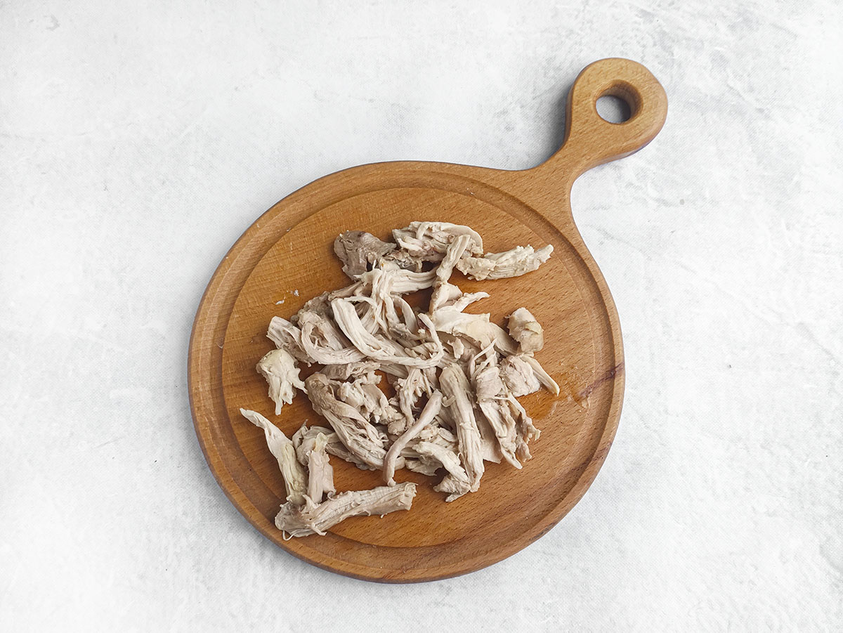 Shredded cooked chicken on a round wooden cutting board.