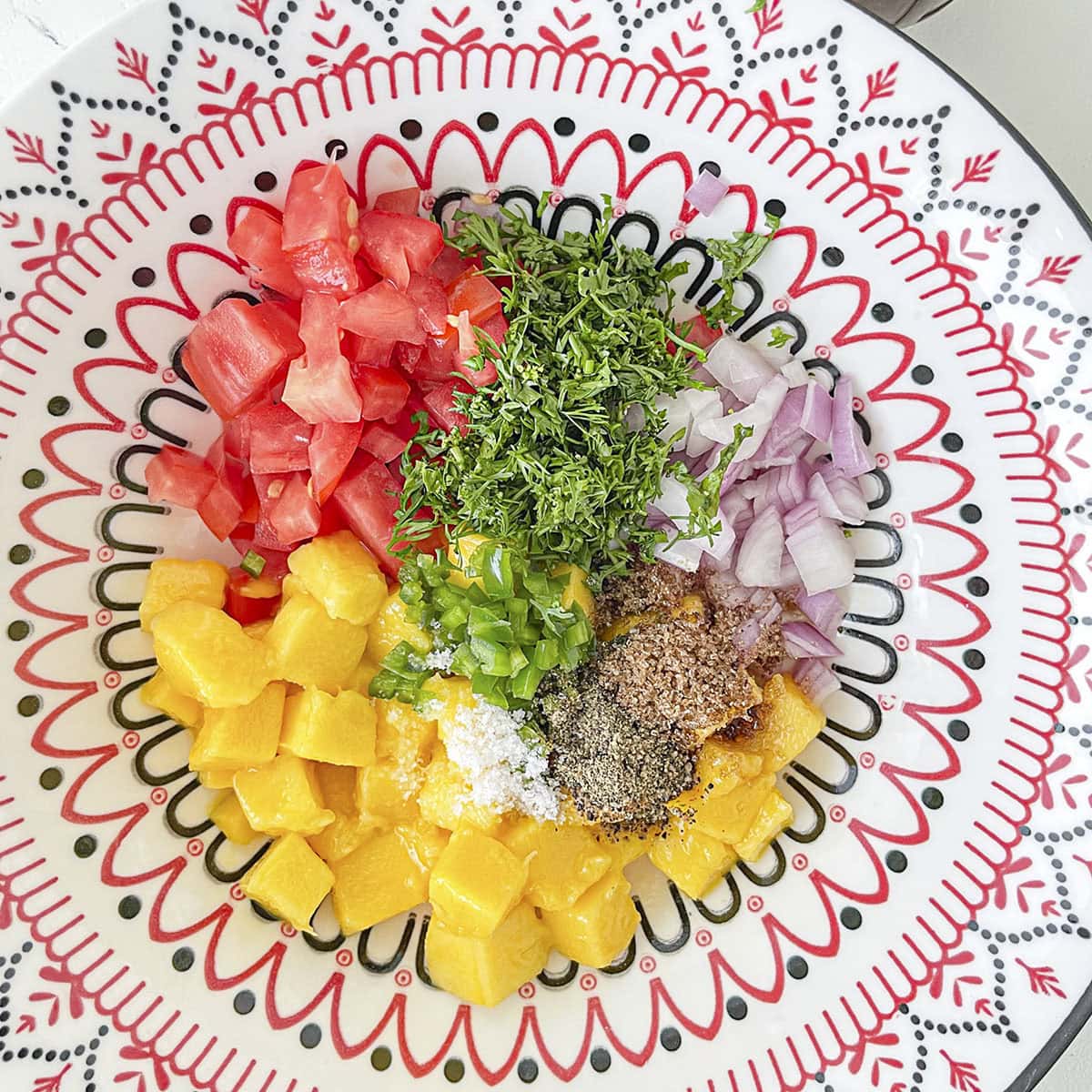 separated piles of chopped salsa ingredients and spices arranged in a decorative bowl before mixing.