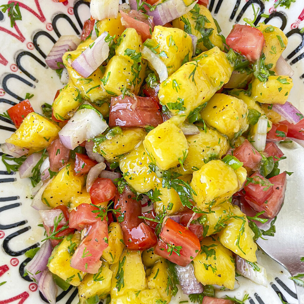 a close-up view of mixed, diced mango, tomatoes, onions, and herbs in a bowl.
