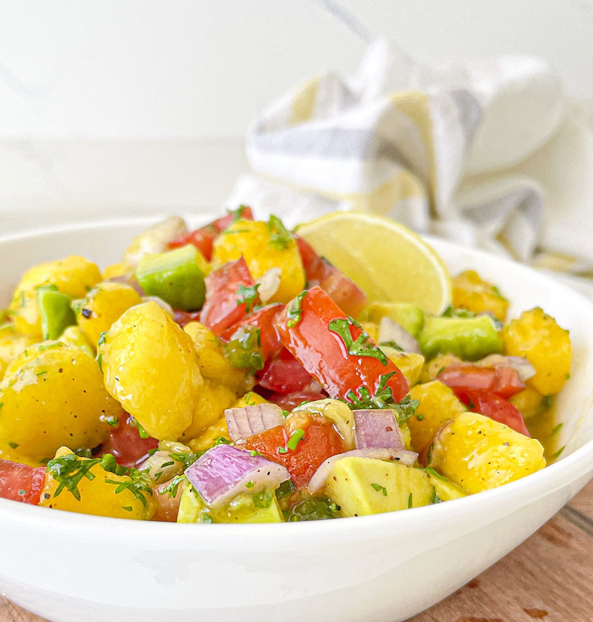 A close-up view of a colorful fruit and vegetable salsa mixed in a white bowl.