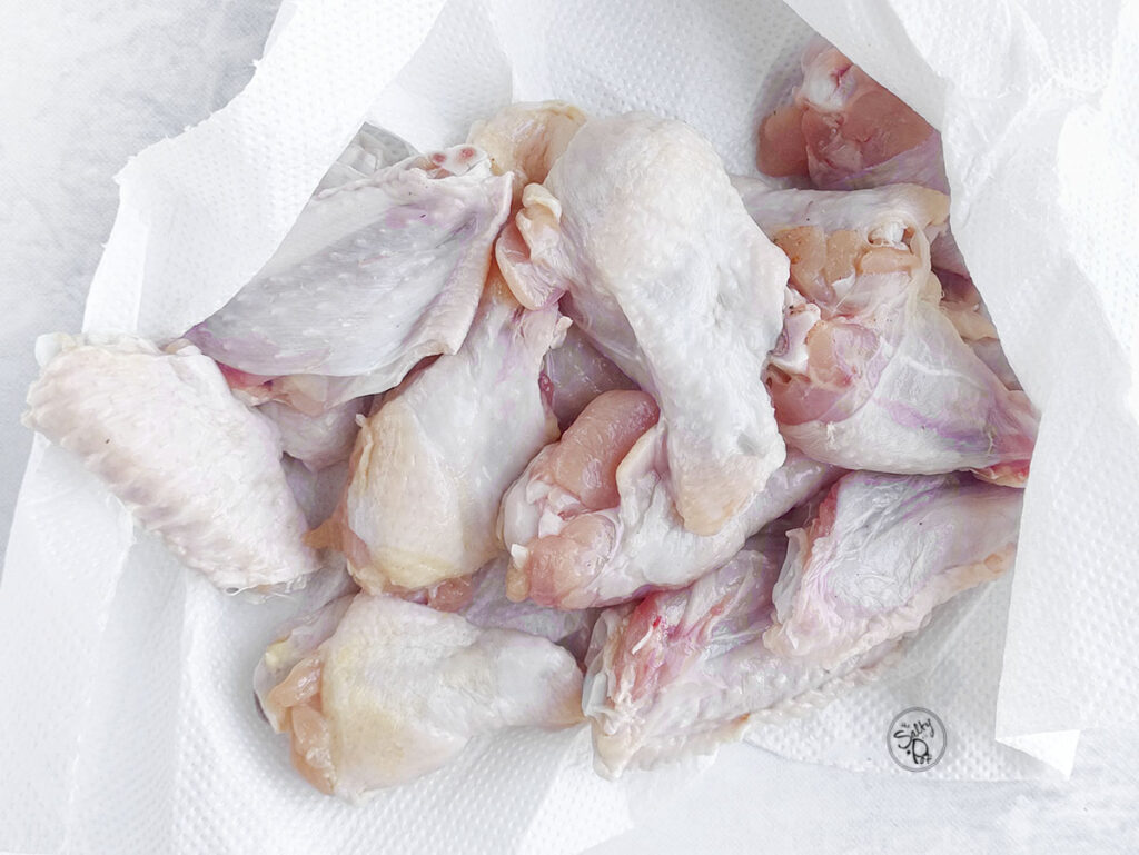 Raw chicken wings patted dry with paper towels on a flat surface.