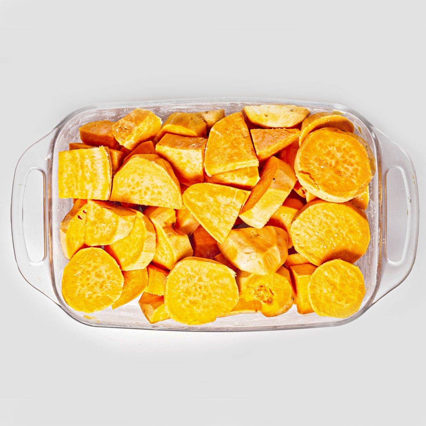 Peeled and sliced raw sweet potatoes tightly packed inside a clear baking dish.