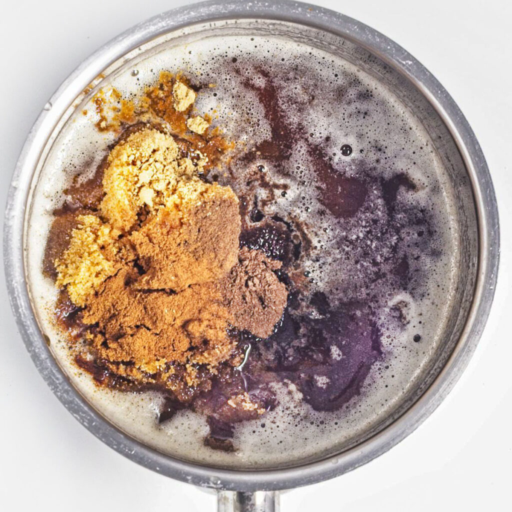 Brown sugar, cinnamon, and spices added to melted butter in a pot.
