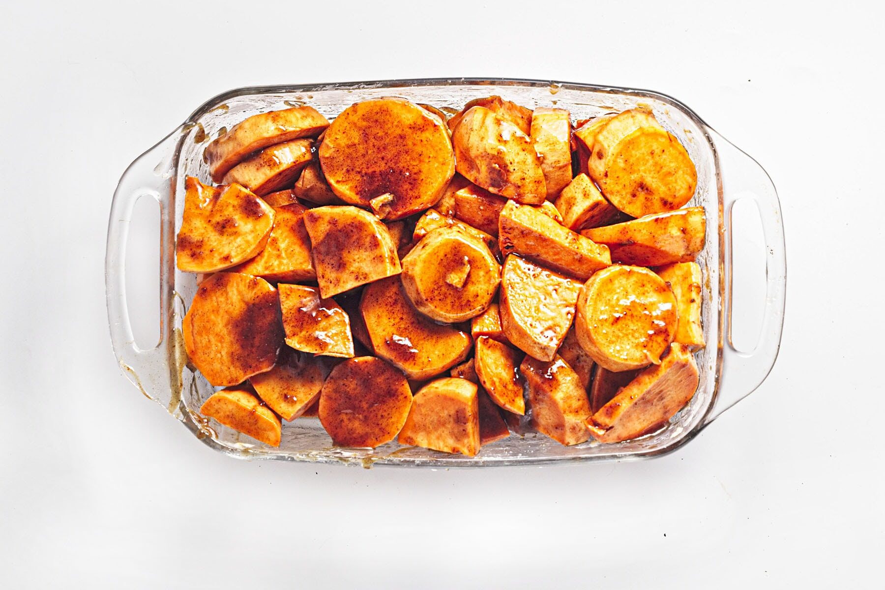 Glass baking dish filled with tender, syrup-coated sweet potato slices on a navy towel.

