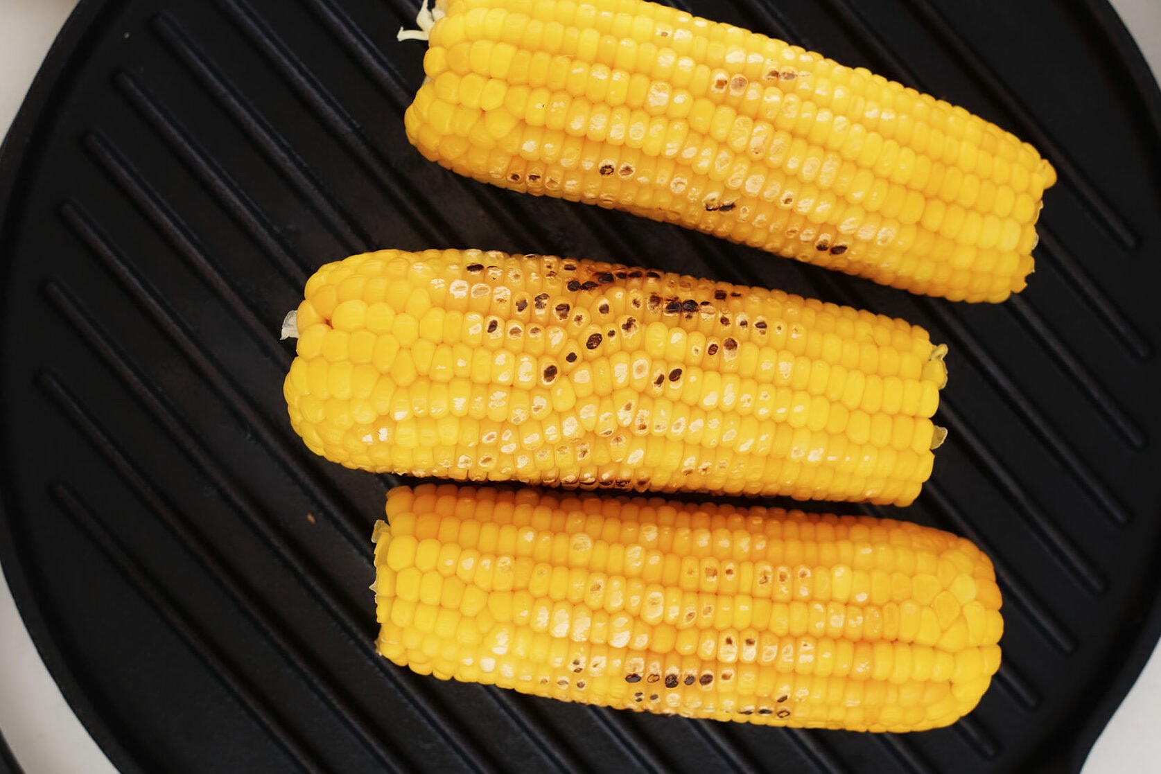 Three cobs of corn with light char marks resting on a black grill pan