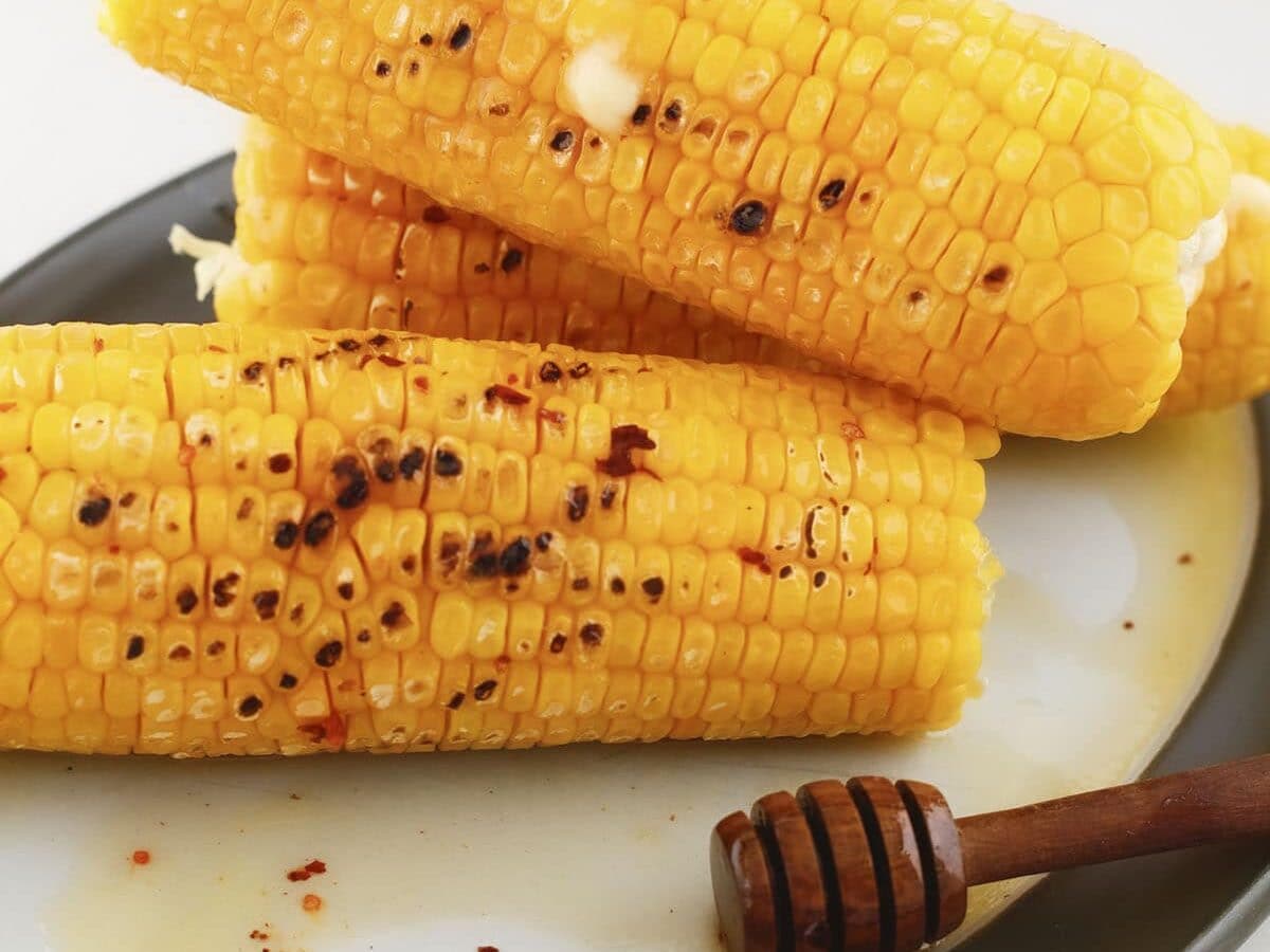Stack of grilled corn on the cob drizzled with hot honey alongside a honey dipper