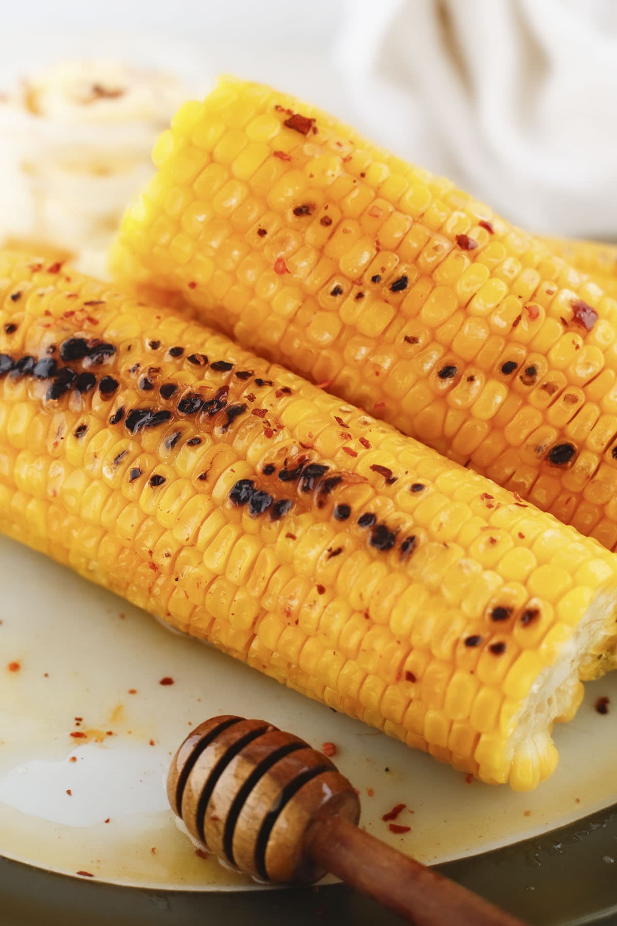 Close-up of grilled corn cobs drizzled with hot honey next to a wooden honey dipper