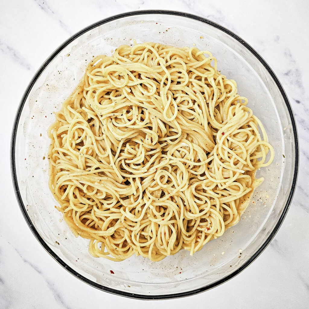 A glass bowl containing plain cooked spaghetti.

