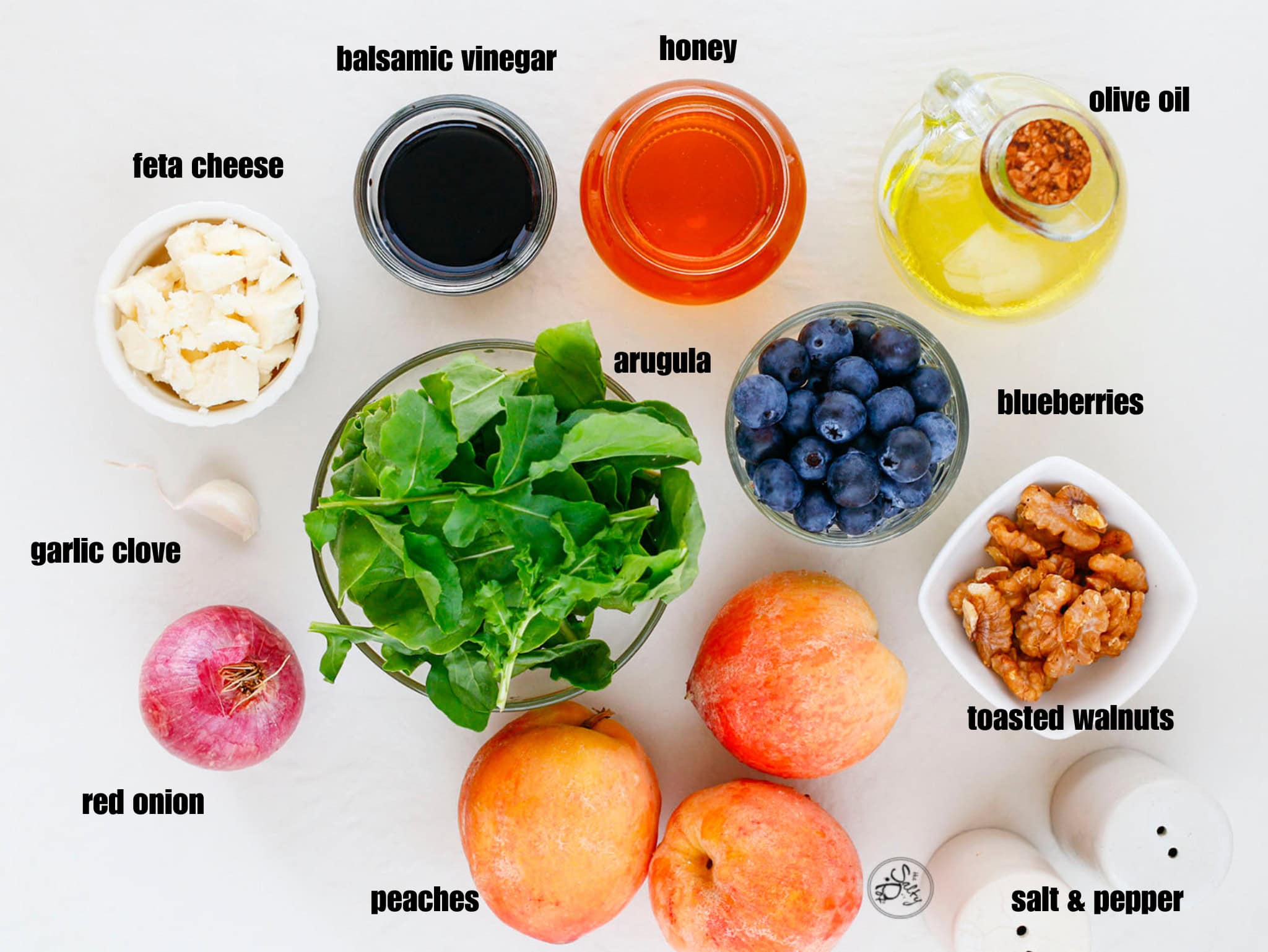 Ingredient image for the peach salad. Arugula in the center, then clockwise, honey, oil, blueberries, walnuts, salt and pepper, peaches, red onion, garlic clove, feta cheese and balsamic vinegar.
