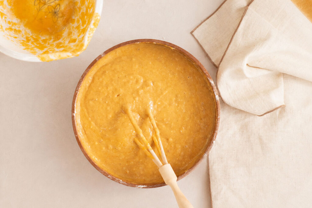 Smooth orange batter being mixed with a whisk in a large ceramic bowl