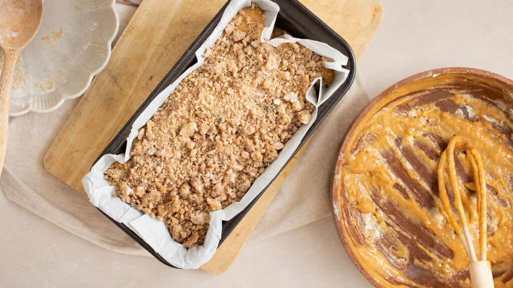 Unbaked cake batter topped with crumble mixture inside a parchment-lined loaf pan