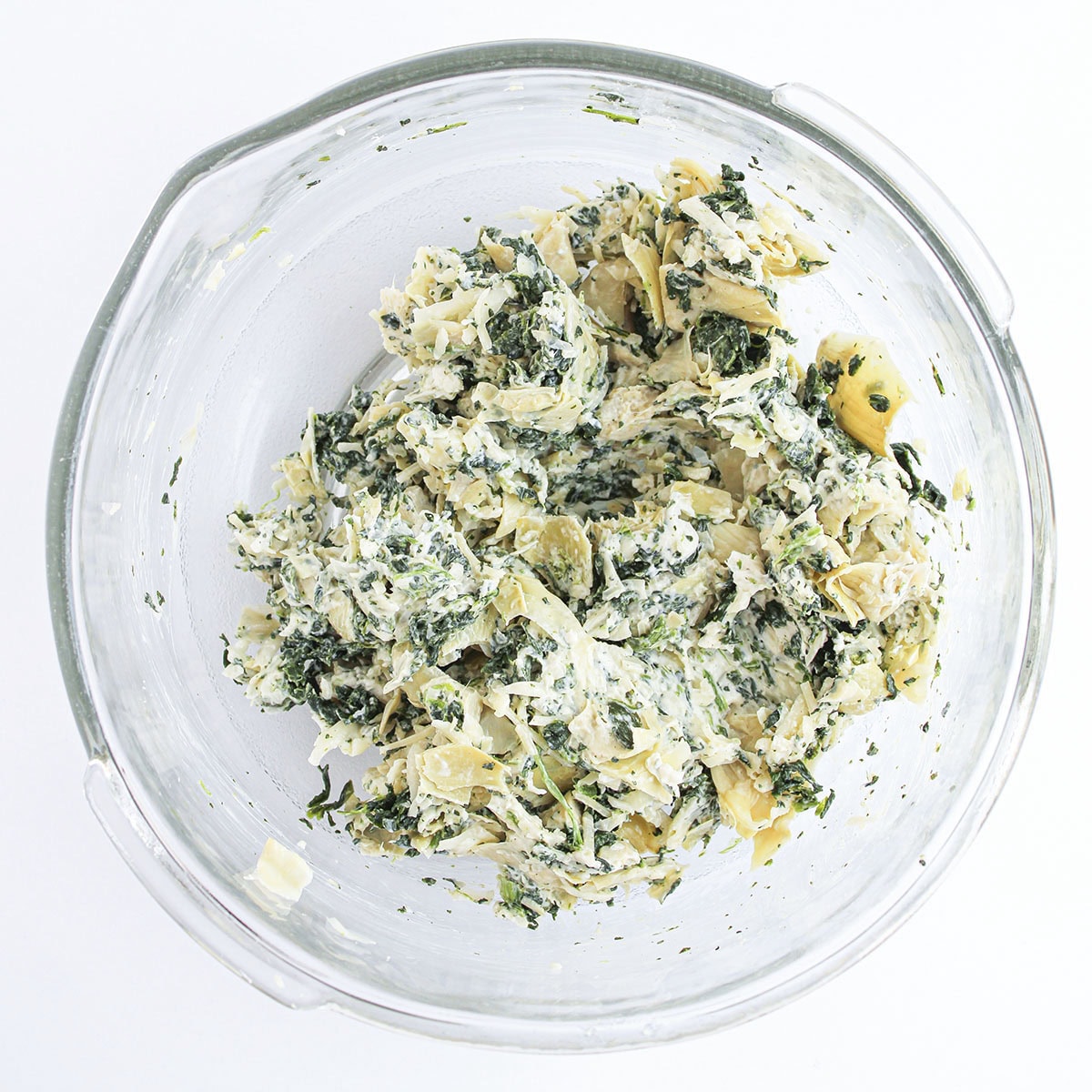 Spinach, chopped artichoke hearts, and cheese mixed together in a clear glass bowl