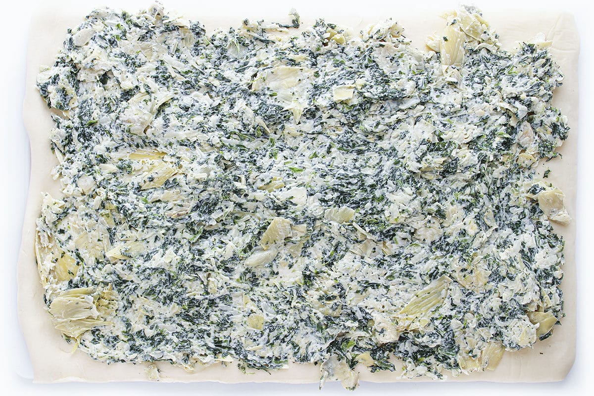 Creamy spinach and artichoke filling spread evenly across a sheet of unbaked pastry dough