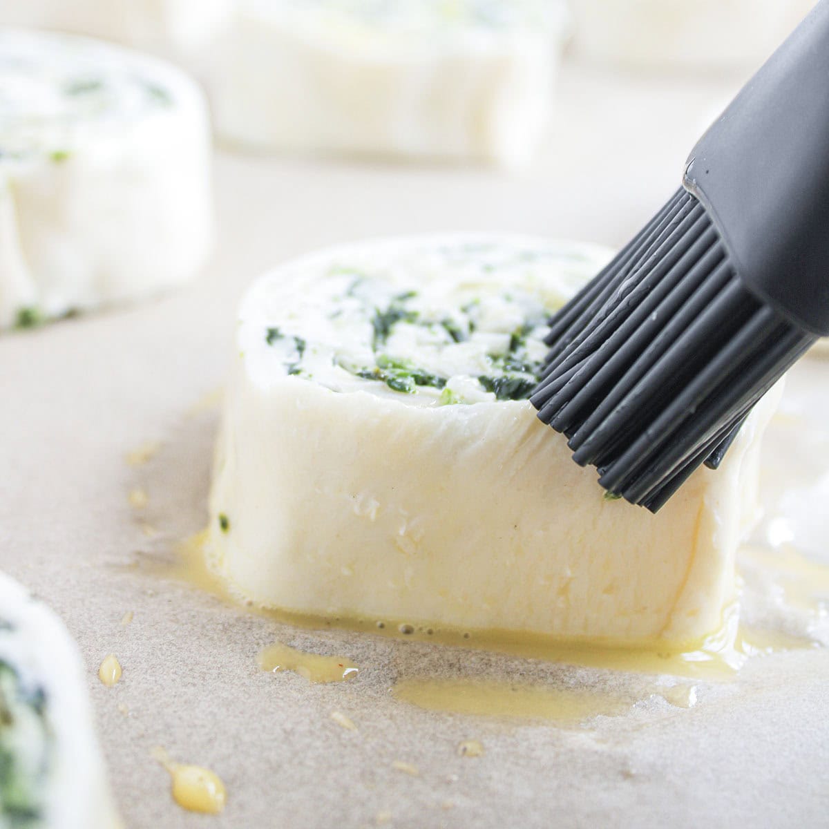 Close-up of egg wash being brushed onto an unbaked pinwheel slice with a black silicone pastry brush