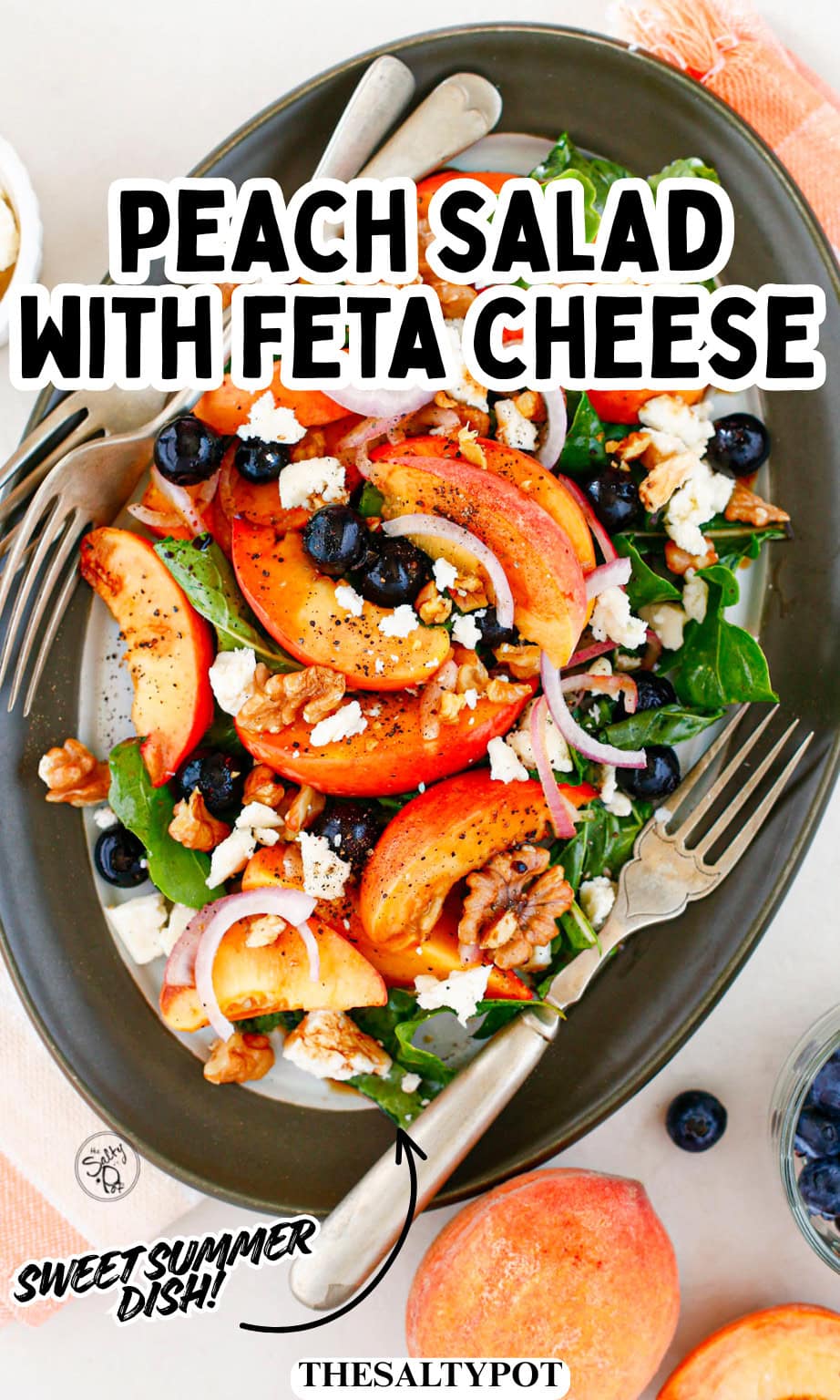 Full view of a fresh peach salad arranged on a dark oval platter next to serving forks.