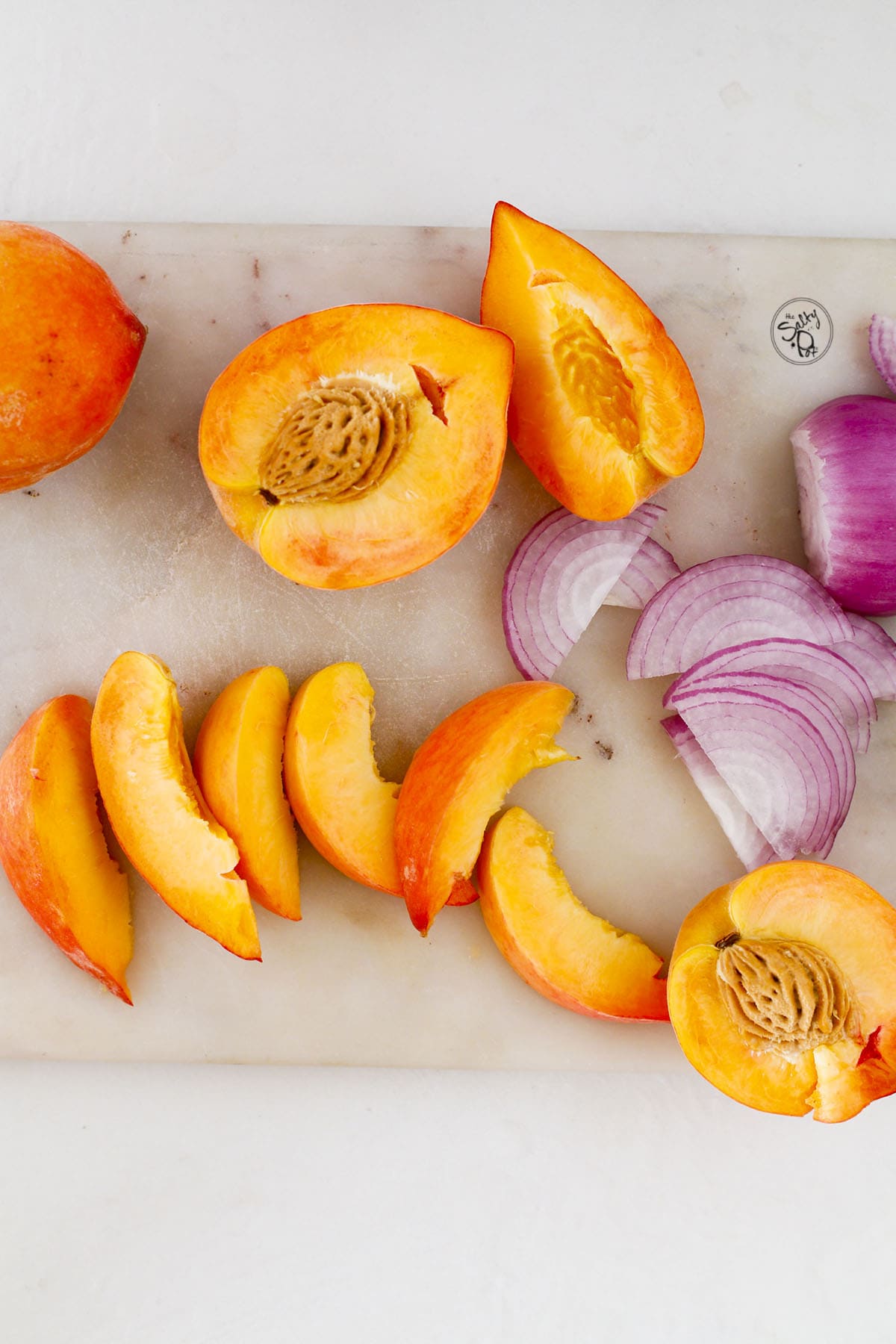 Sliced fresh peaches and red onion on a light-colored board.