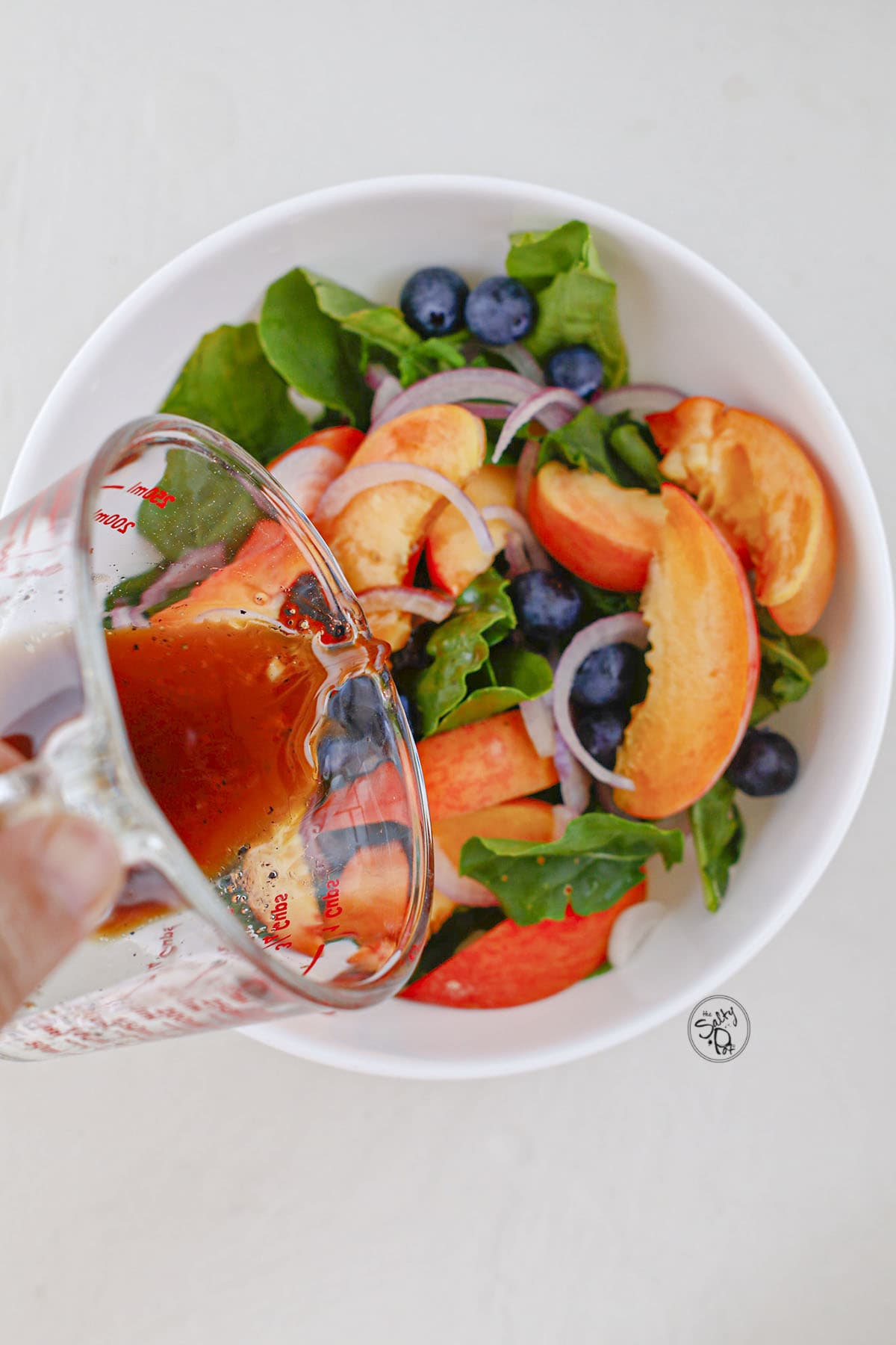 Pouring liquid dressing from a glass cup into a bowl of salad.