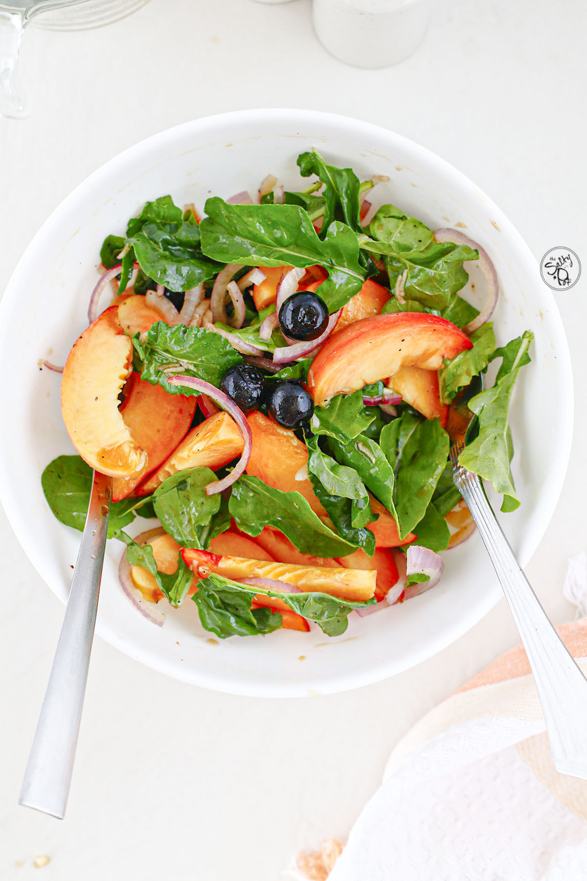 Peach salad mixed in a white bowl with serving utensils.