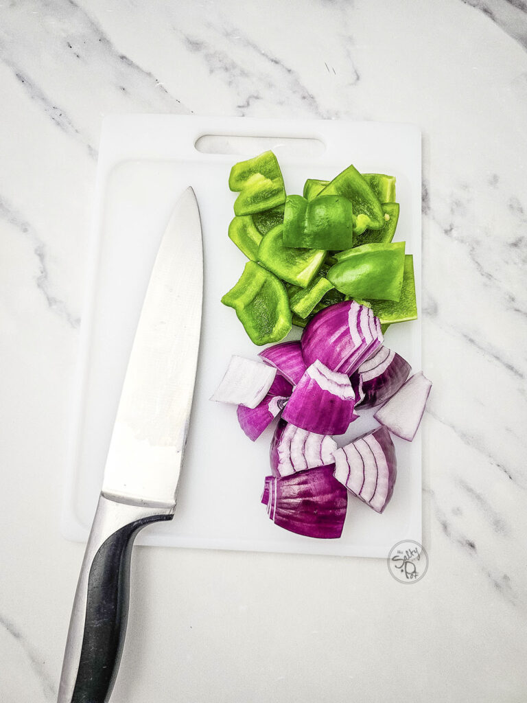 Chopped green bell pepper and red onion chunks on a cutting board next to a knife