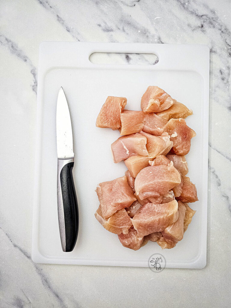 Cubed raw chicken breast next to a chef's knife on a white cutting board