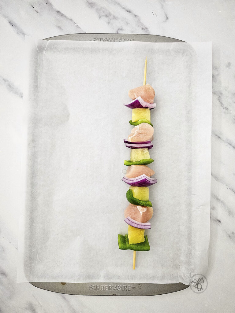 A single assembled wooden skewer with raw chicken, pineapple, green pepper, and red onion