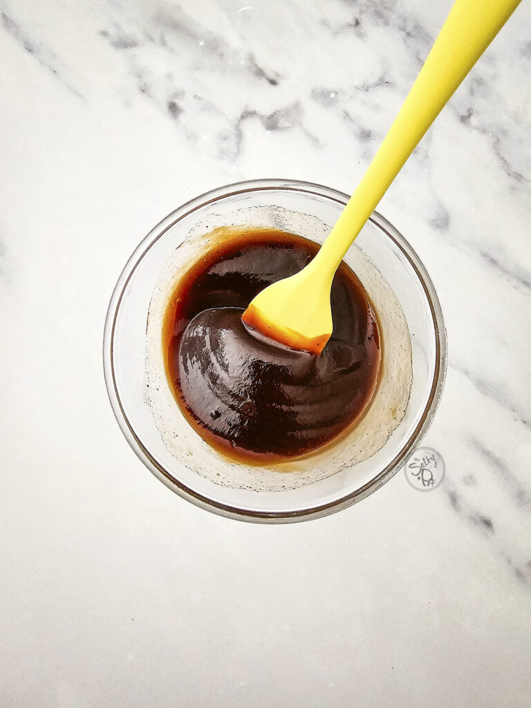 Small glass bowl of dark teriyaki marinade with a yellow spatula