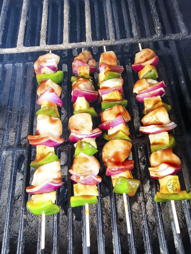 Raw chicken and vegetable skewers grilling on barbecue grates