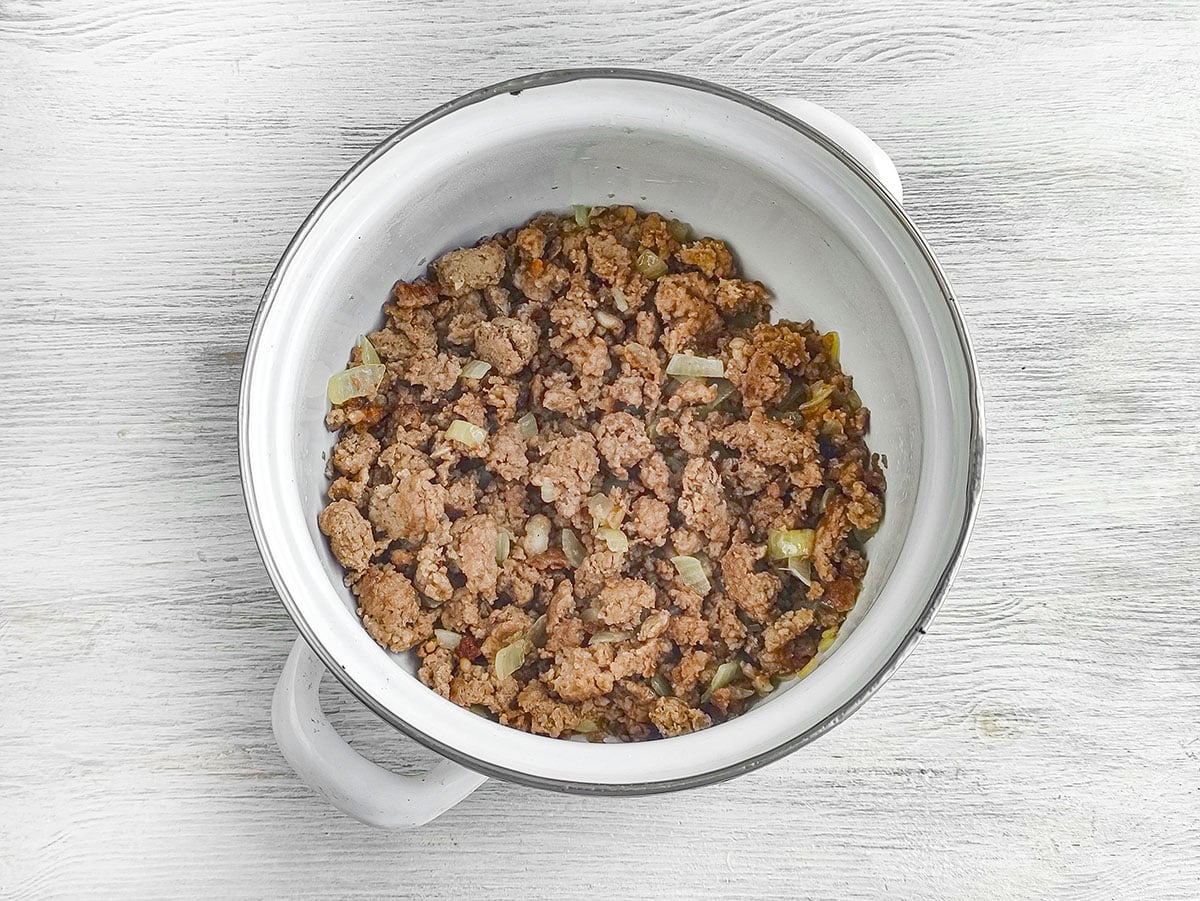 Cooked ground meat and onions at the bottom of a white cooking pot