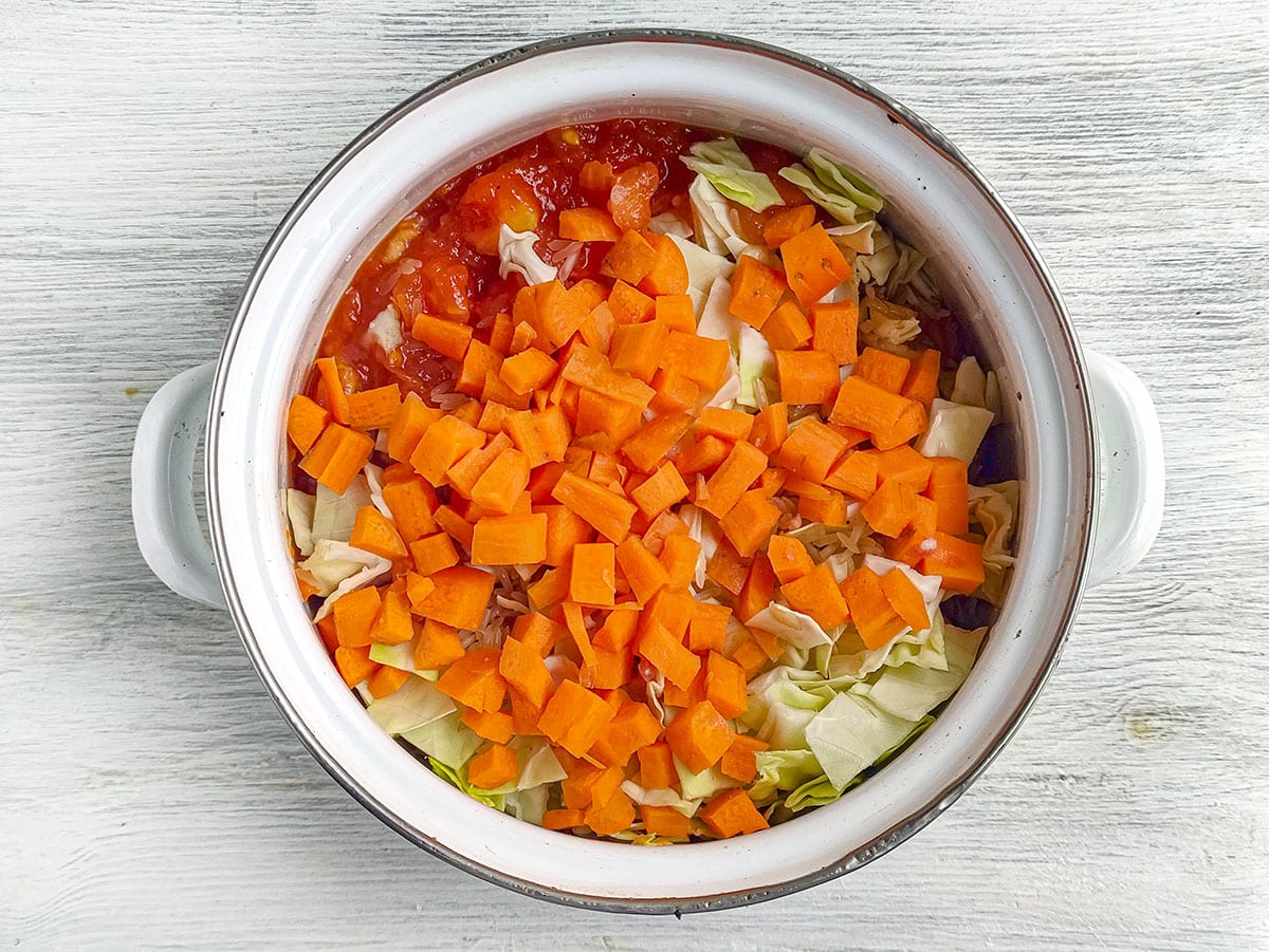 Diced carrots, chopped cabbage, and tomato sauce layered inside a pot before cooking