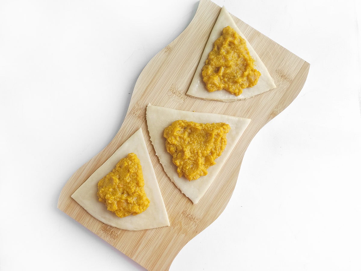 Triangular pieces of dough topped with scoops of orange filling on a wooden board