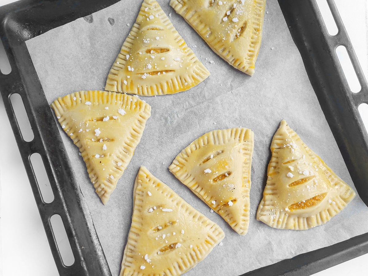 Unbaked dough turnovers brushed with egg wash and lined up on a parchment-covered baking sheet